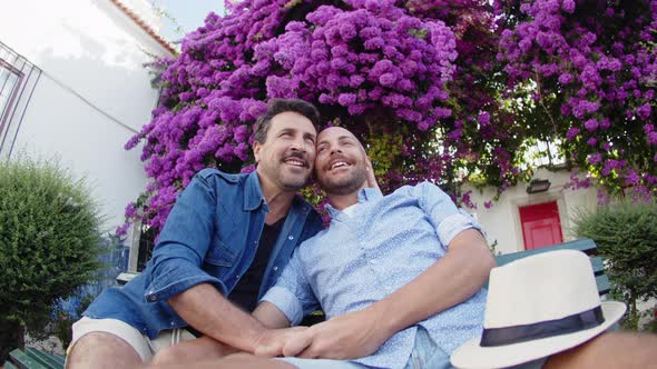 Front View of Gays Kissing on Bench in Park with Blooming Trees alt