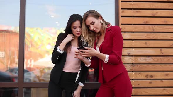 Two Gorgeous Young Women in Suits Browsing Phone with Smile and Laughter