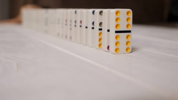 White Dominoes with Multicolored Dots Slowly Fall on a Light Wooden Background alt
