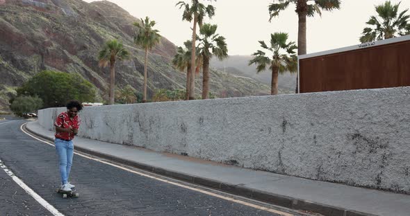 African american man riding a longboard on the road with palm trees in the background alt