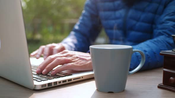 Close up Cup of coffee with smoke on desk table with man using laptop background in morning. alt
