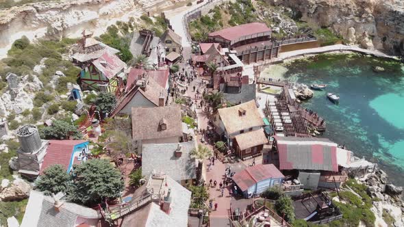 Aerial fly over shot of Popeye Village fun park Main Route full of tourists on Anchor Bay, in Malta alt