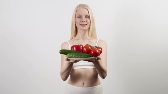 A Young Slender Blonde Woman Holds a Plate with Cucumbers and Tomatoes in Her Hands