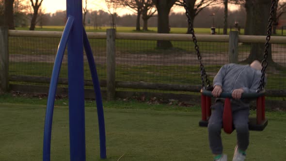 Medium Plan of Funny Little Preschool Chubby Girl In Pink Jacket Swinging On Swing Before Sunset alt