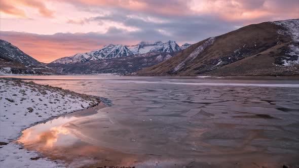 Time lapse over frozen lake looking at snow capped mountains during sunset alt