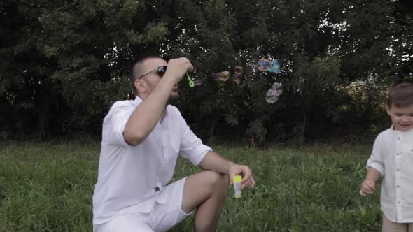 Young Father Blows Bubbles for His Happy Child in the Park