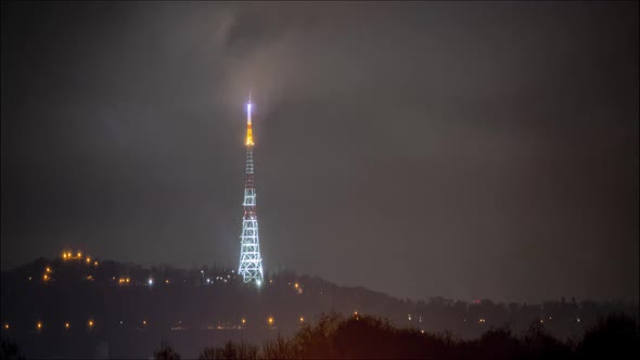 Beautiful night time lapse: illuminated television tower covered by stormy clouds.
