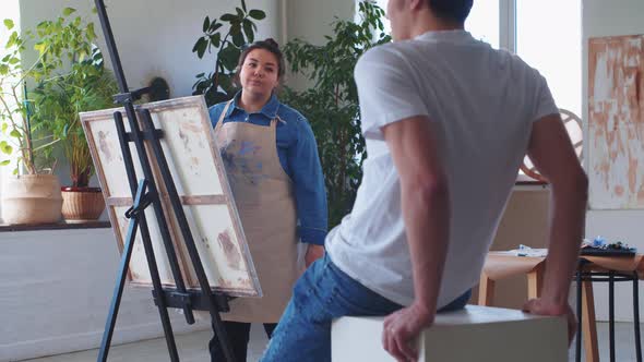 A Woman Paint Artist Drawing on a Canvas Taking a Male Model As a Reference alt