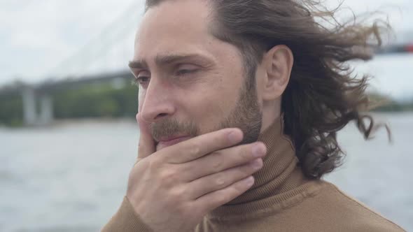 Close-up Face of Frustrated Young Man with Sore Eyes Standing Outdoors on Windy Day. Portrait of alt