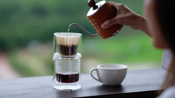 A woman pouring hot water from kettle to make drip coffee with blurred nature background