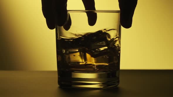 Man Hand Hold Glass with Whiskey. Glass with Whiskey Rotating at Wooden Table. alt