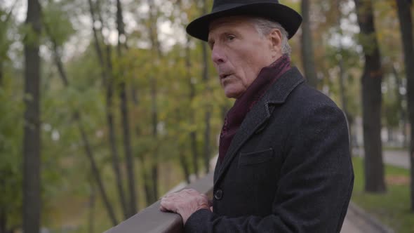Side View of a Troubled Caucasian Man Approaching Handrails in the Autumn Park and Looking Away alt