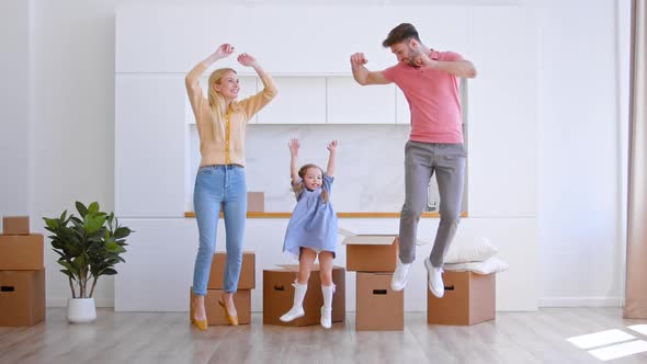 Happy new apartment owners family with little girl jump on brown wooden floor alt