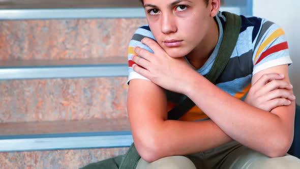 Sad schoolboy sitting alone on staircase alt