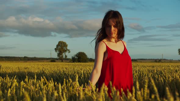 Young Woman in a Red Dress Walks Across the Field with Rye