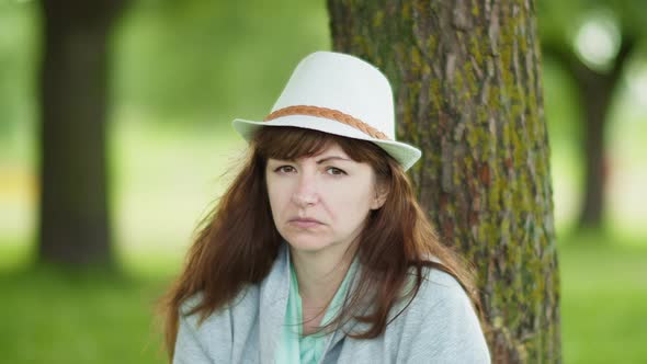 Portrait of a Serious Brunette Woman in a Hat in the Park Looking at the Camera