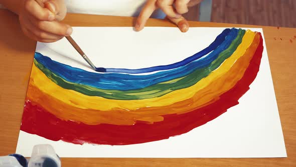 A Child's Hand Draws a Large Rainbow with Colored Paints on a Sheet alt