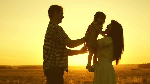 Family with a Kid in a Field in the Sunset Light. Father, Daughter and Mother Are Playing alt