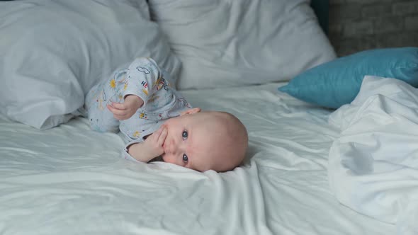 baby with hand in mouth lies on the bed