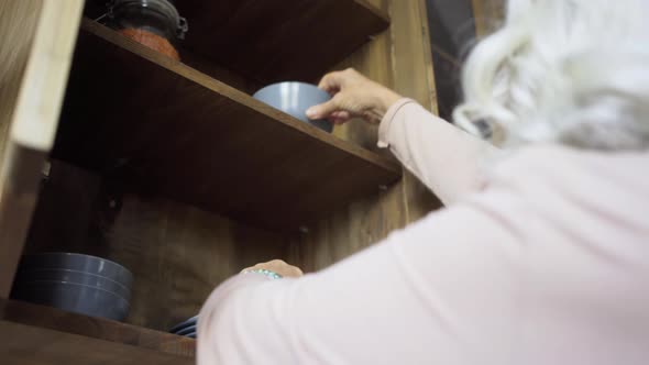 Aged Lady with Blue Bracelets Puts Bowls Plates in Cupboard