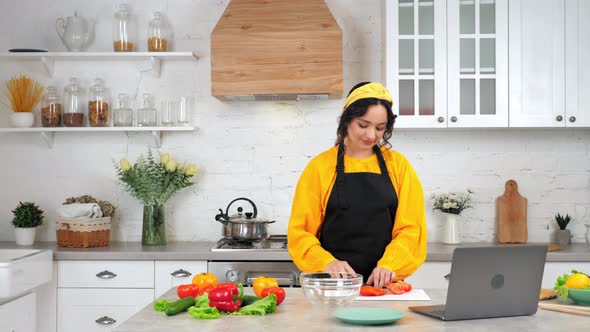 Smiling Woman Housewife Slices Tomato Listen Chef Study Online Video Call Laptop alt