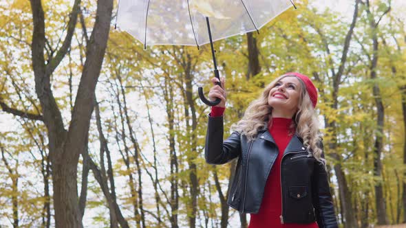 Beautiful Blonde Woman Raises an Umbrella with Leaves and They Fall Down alt