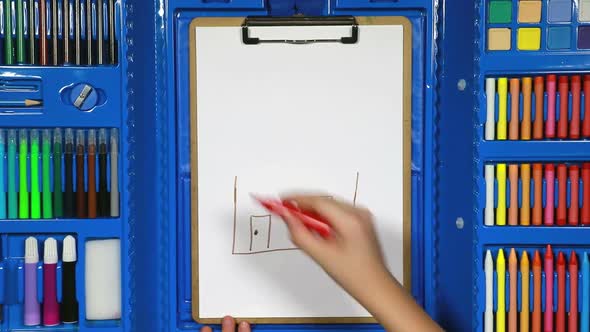 The Girl's Hand Draws a Child's Drawing With a House Using Various Markers