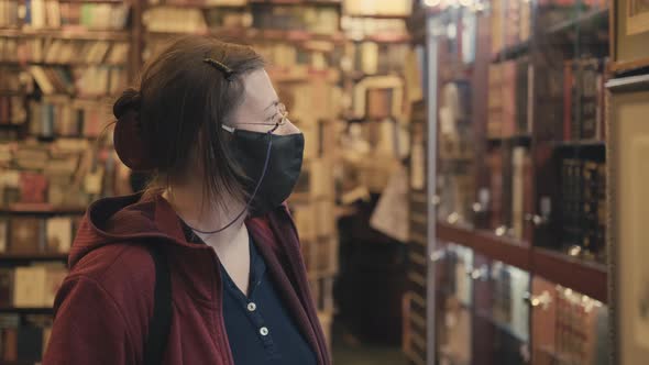Woman in Glasses and Mask Against Virus Chooses Painting to Buy in Antique Shop