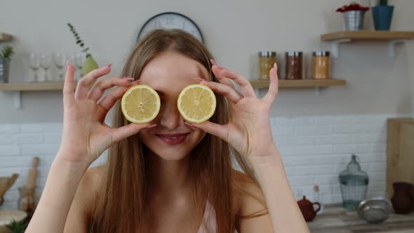 Joyful Young Girl Vegan Holding Fresh Halves of Lemon on Eyes and Fooling Around, Making Funny Faces alt