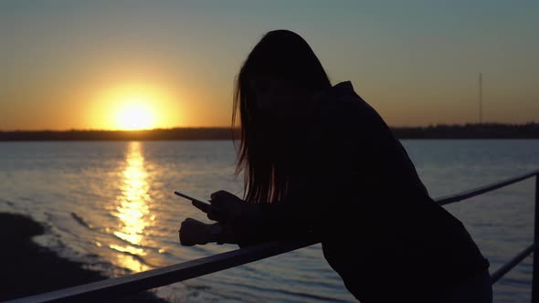 Woman on Pier Using Smartphone Silhouette on Suset Evening Walking Outdoor