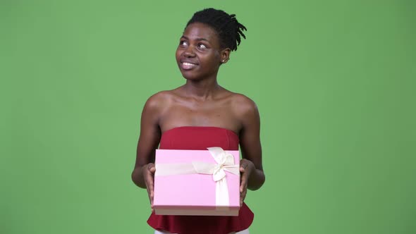 Young Beautiful African Woman Thinking While Holding Gift Box
