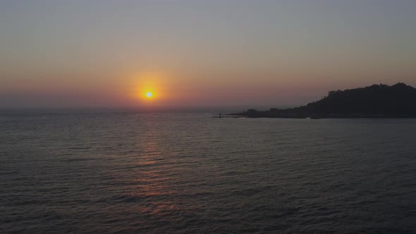 A seascape at sunset, where you can see the island, breakwater, and lighthouse alt