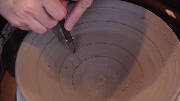 A Woman Carves a Pattern on a Clay Plate Using a Tool alt