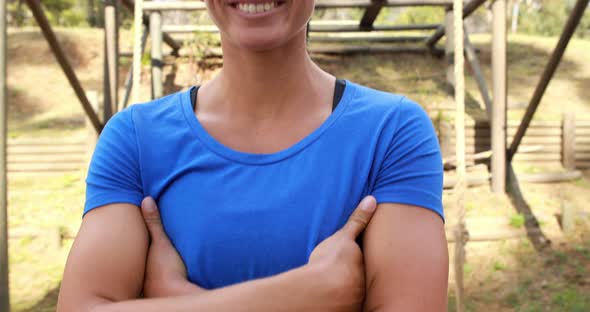 Smiling fit woman standing with arms crossed in park alt