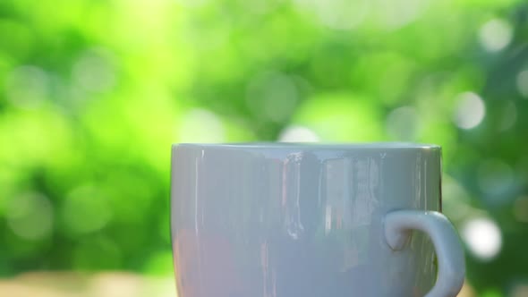 Hot Drink in a Cup Against the Background of a Summer Garden in the Morning alt