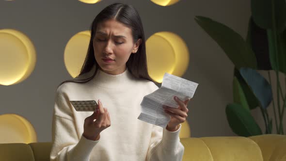 Young Asian Woman Holds a Blister Pack of Pills and Reads Medical Instructions alt