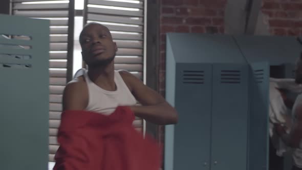 Athletic Black Man Taking off Hoodie at Locker Room and Chatting with Friend alt