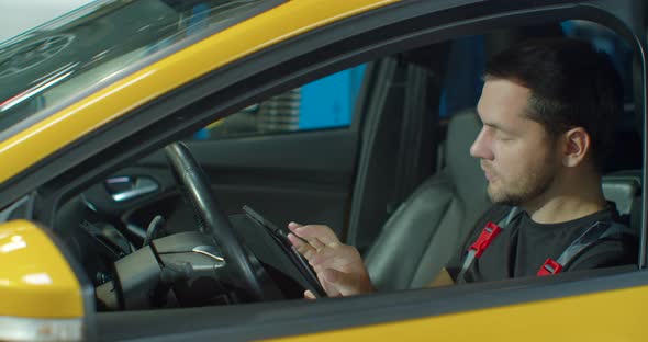 Mechanic Sitting in Car Doing Diagnostics on Digital Tablet alt
