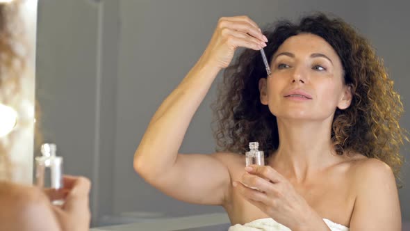 Wellgroomed Mature Woman After a Shower Apply a Cosmetic Serum to the Face with a Pipette alt