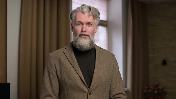 Stylish gray-haired man with a beard talking while transmitting a video message alt