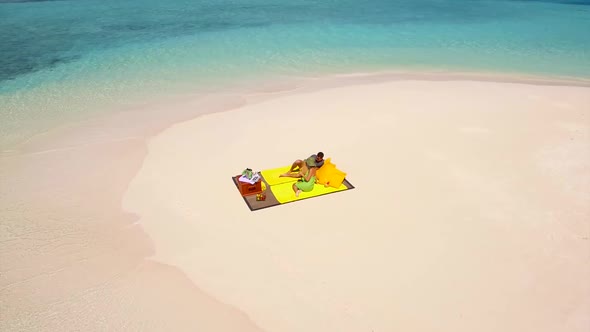 Aerial drone view of a man and woman couple having a picnic meal on a tropical island beach alt