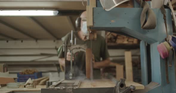 Carpenter slicing a wooden block with a saw machine
