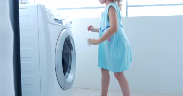 Little Girl Loads the Laundry in the Washing Machine and Includes Washing alt