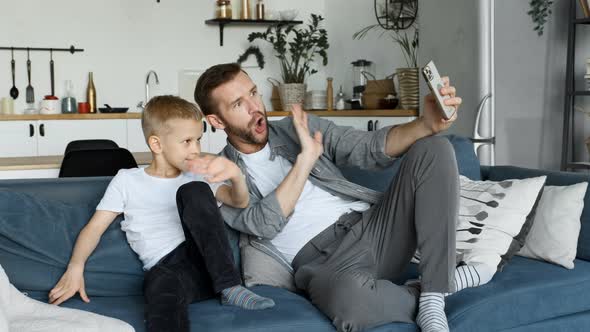 Father and Child Look at the Smartphone Screen and Communicate Online with Friends, Relatives or Mom alt
