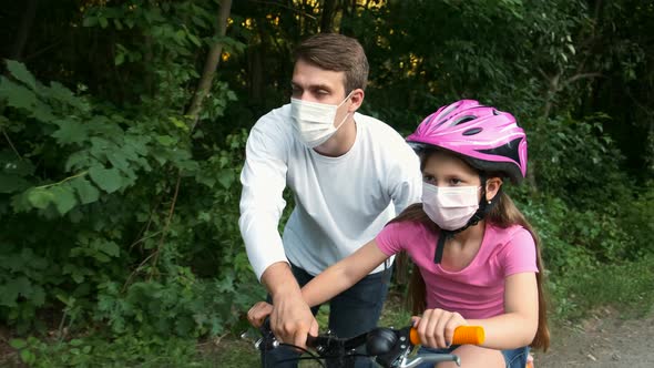 A young father teaches his daughter to ride a Bicycle in medical masks and a Bicycle helmet. 