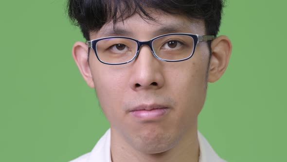 Head Shot of Young Asian Businessman Against Green Background alt