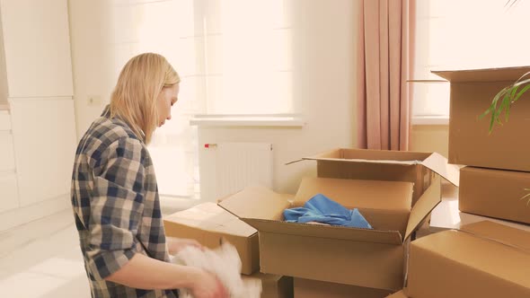 A Tired Young Woman Sits on the Floor and Puts Things in Boxes