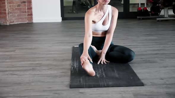 Young Caucasian Woman in Sportswear Sits in Lotus Pose with Closed Eyes on Mat