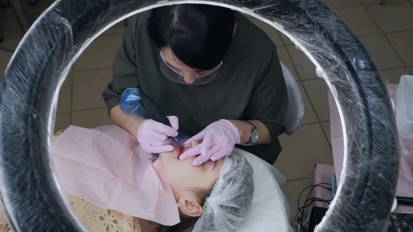 A Beautician Wearing a Mask and Gloves Applies Permanent Makeup to the Lips of a Young Girl