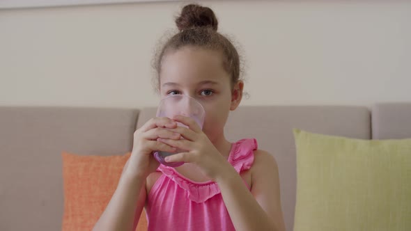 Cute Little Girl Drinking a Glass of Milk in the Kitchen at Home alt